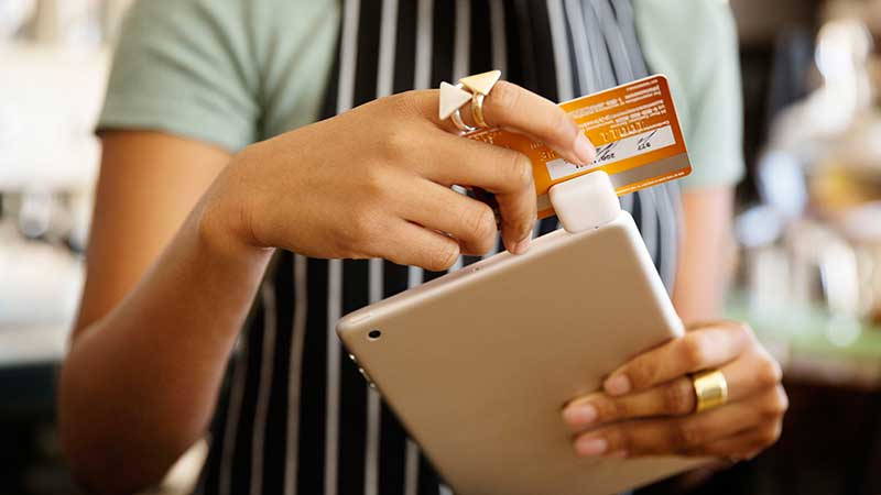 A waitress swipes a Visa card through a Square reader attached to a tablet.